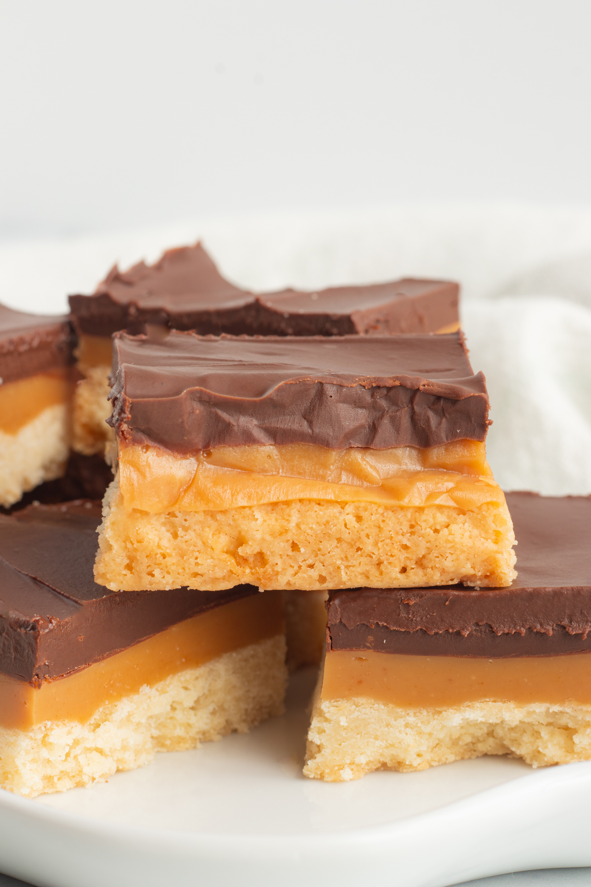 Enjoy a slice of rich, decadent Millionaire Shortbread, also known as Caramel Squares or homemade Twix Bars! This dessert contains three layers of sweetness, including buttery shortbread, gooey caramel filling, and smooth milk chocolate, just like a Twix Bar, but better! Treat yourself to a caramel square any time you want a sweet, indulgent treat! via @foodhussy