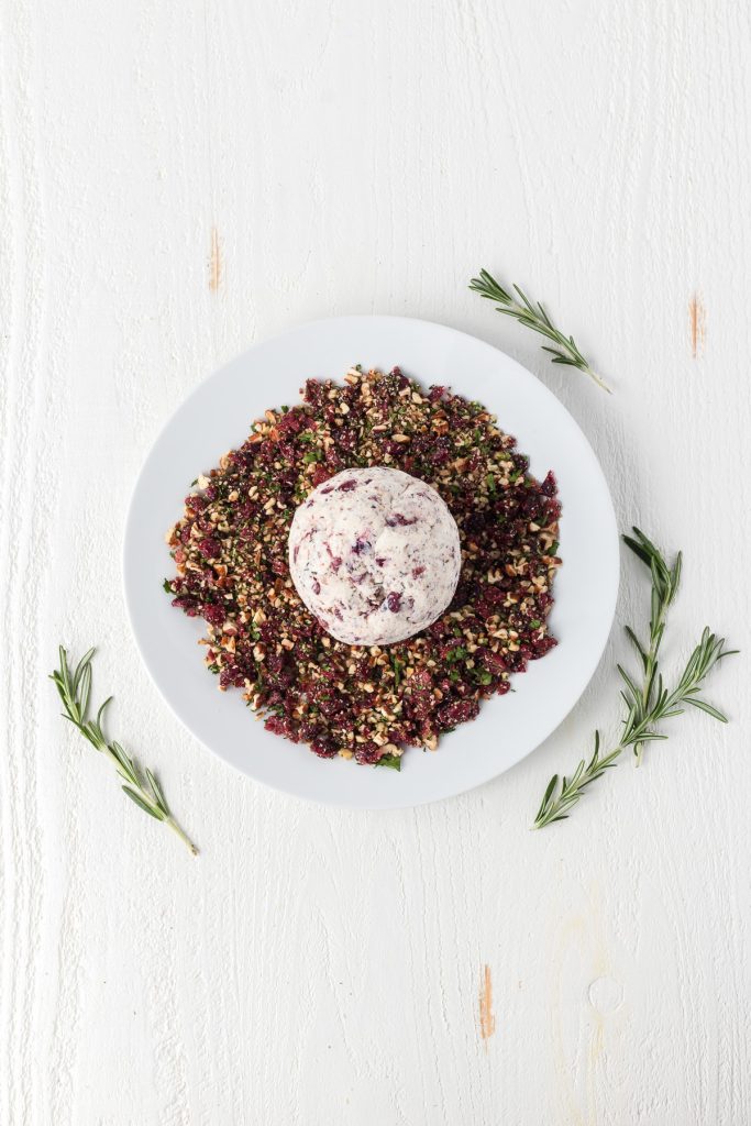 Coating a ball of cheese in chopped cranberries, pecans, and parsley.