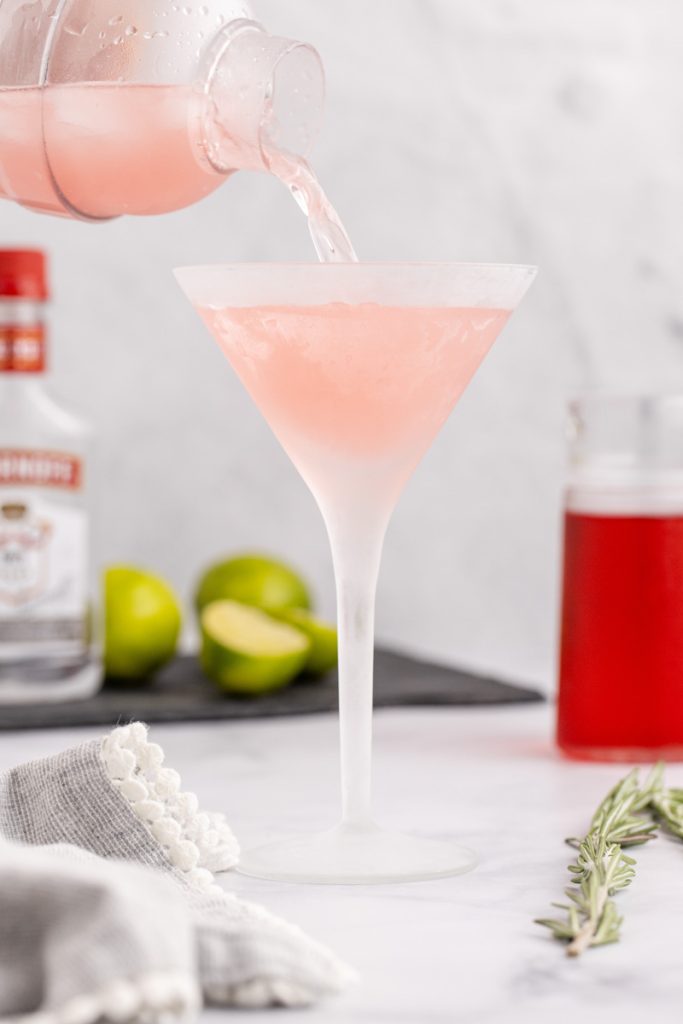 Pouring a cosmopolitan into a glass.