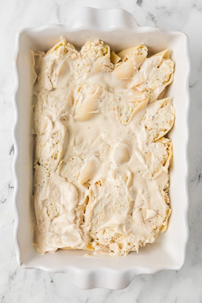 Alfredo sauce on top of stuffed shells awaiting a sprinkling of cheese.